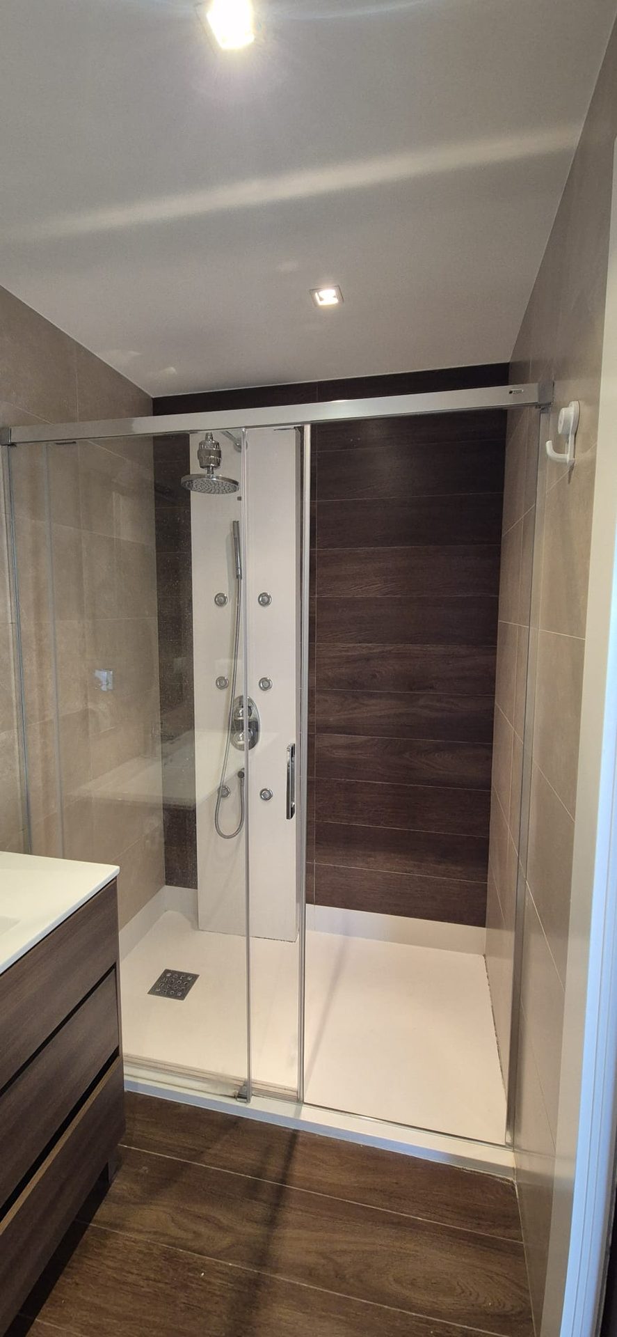 Ducha reformada con panel efecto madera y mampara de cristal